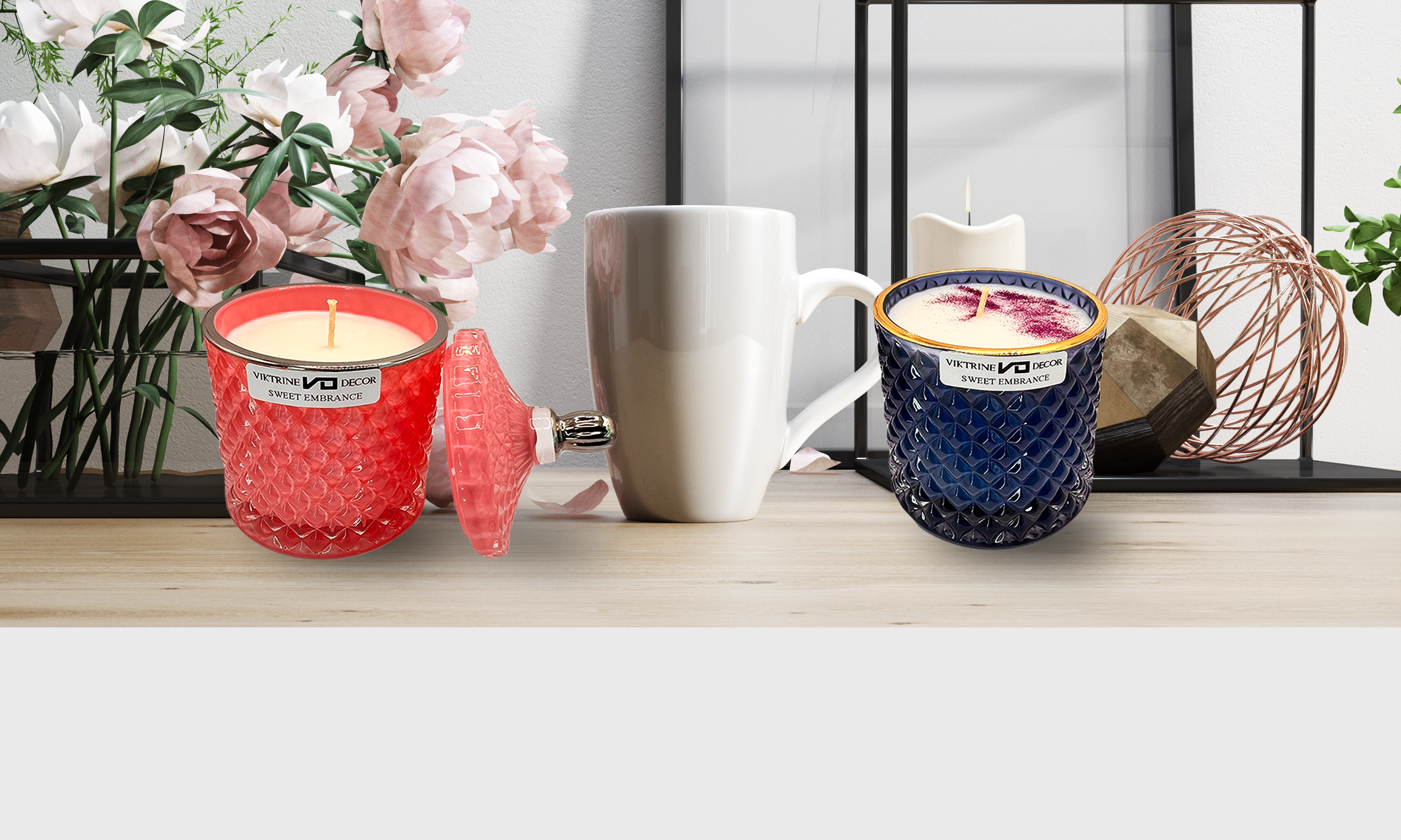 Two candle jars on a table, accompanied by a tea cup and floral decor